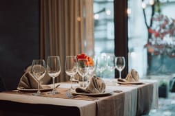 Elegant restaurant table set with wine glasses, plates, and folded napkins—perfect inspiration for catalog resources. A small flower arrangement sits in the center, while large windows reveal a tranquil view of trees outside.