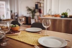 A dining table with empty plates, wine glasses, cutlery, a small bowl of salad, and a yellow patterned table runner in a modern kitchen setting—perfect for showcasing Catalog Resources and inspiring fresh décor ideas.