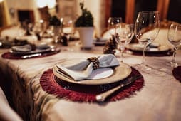 A formal dining table is set with plates, napkins, cutlery, wine glasses, and centerpiece plants from Catalog Resources, creating an elegant atmosphere.