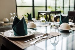 Table set for a meal with plates, folded napkins, glasses, bowls, and cutlery arranged neatly in a bright, modern dining area—perfect for showcasing Catalog Resources.
