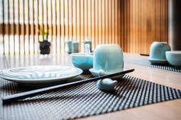 A minimalist table setting with blue ceramic dishes, chopsticks, and a cup on a woven placemat, styled as if curated for Catalog Resources, with soft natural light in the background.