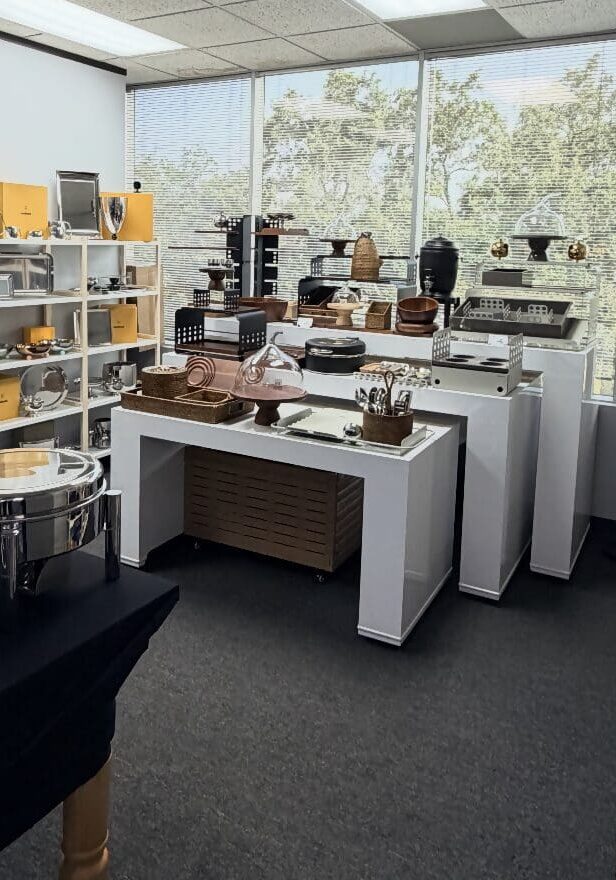 Showroom with shelves and tables displaying various kitchenware items, including pots, pans, dishes, and utensils, in a well-lit room with large windows.
